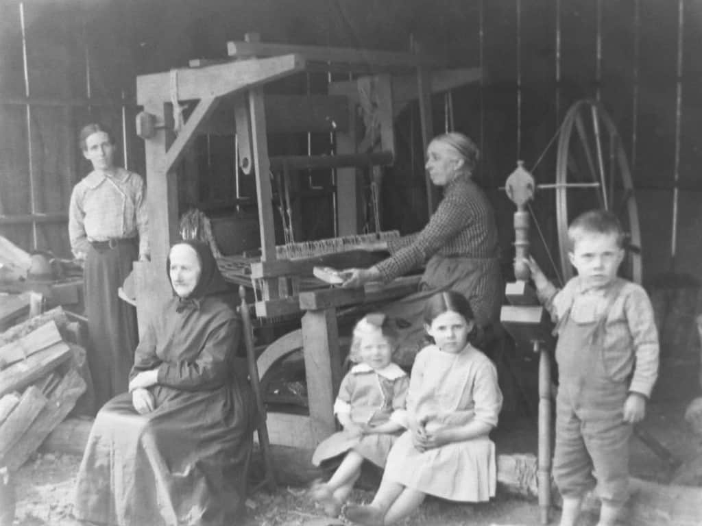 Photograph showing Mary Harman at her loom with family members around her.